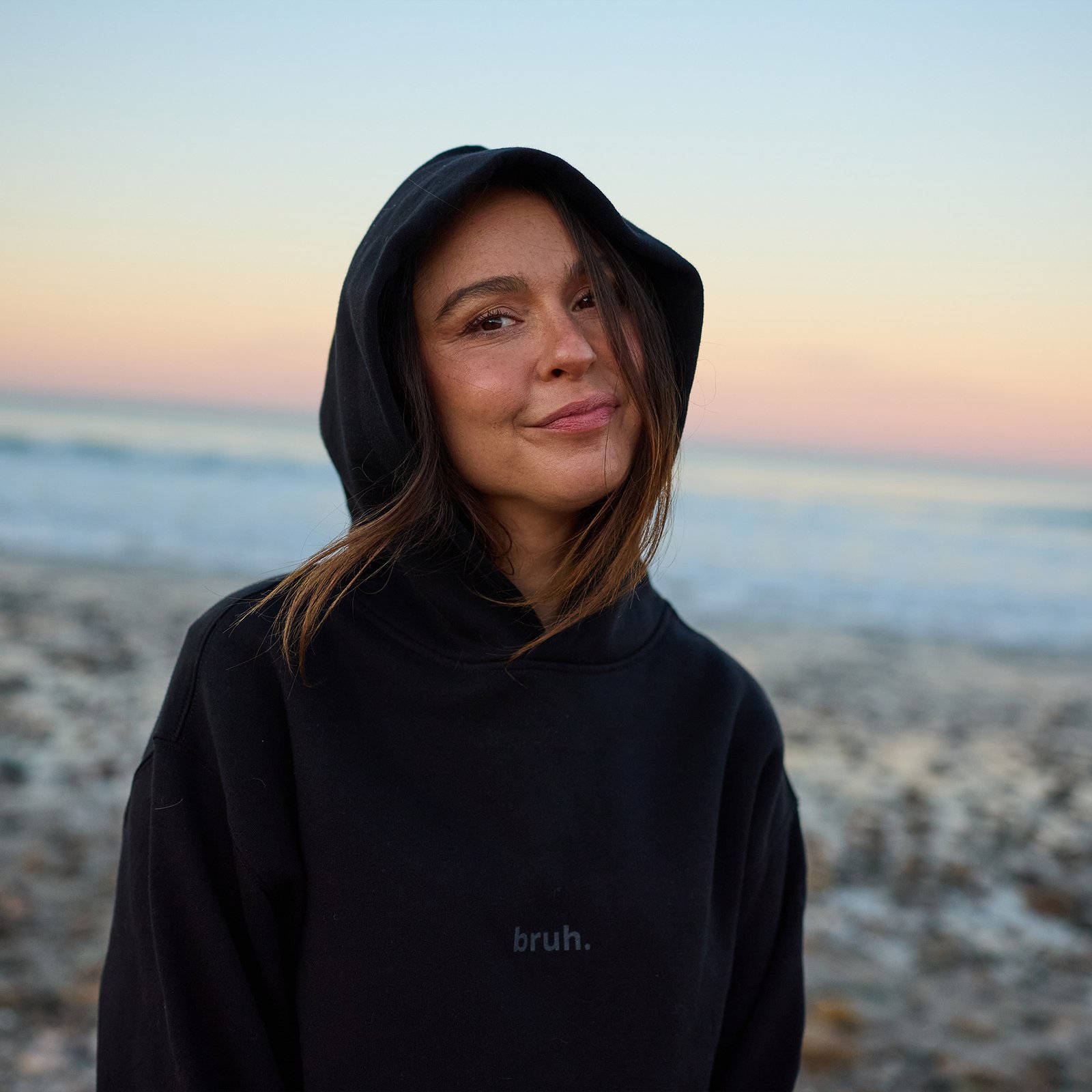 Portrait wearing a black Sloopy Brand hoodie at sunset on the beach.